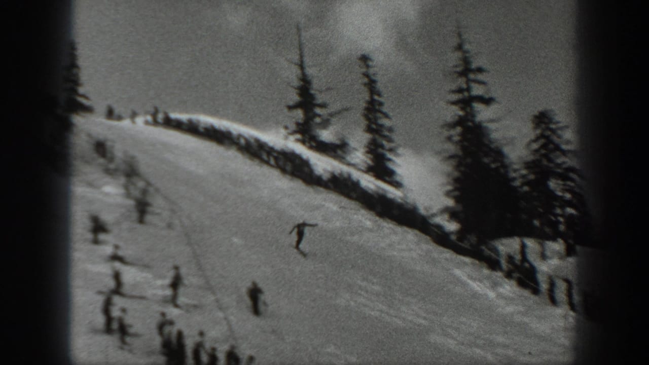 Skier airborne on a snowy ski jump slope with people below and trees nearby.