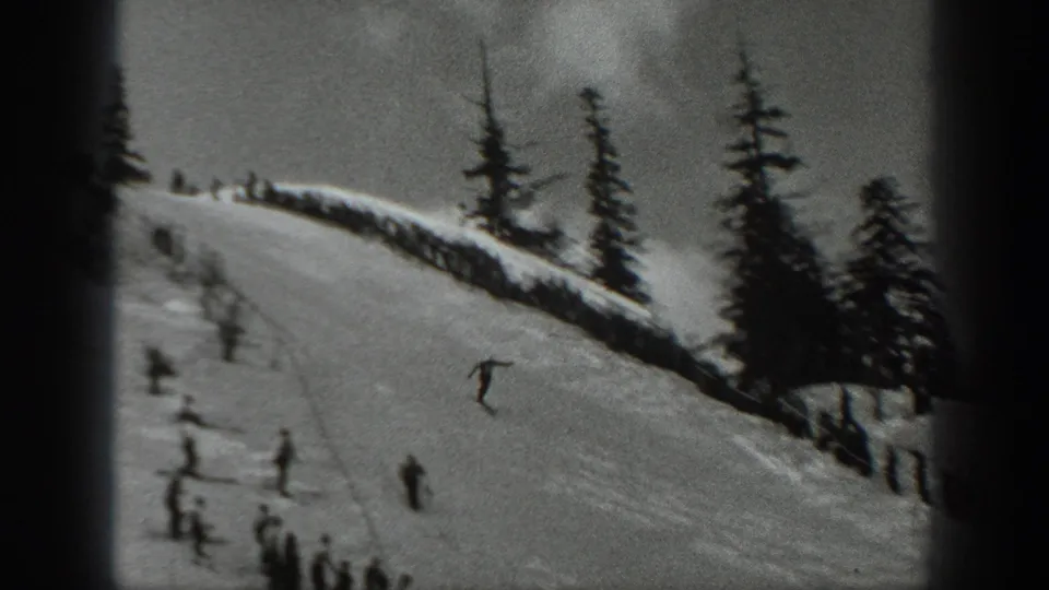 Black-and-white 1940 Washington frame of a skier mid-jump above a snowy slope with small figures watching below.