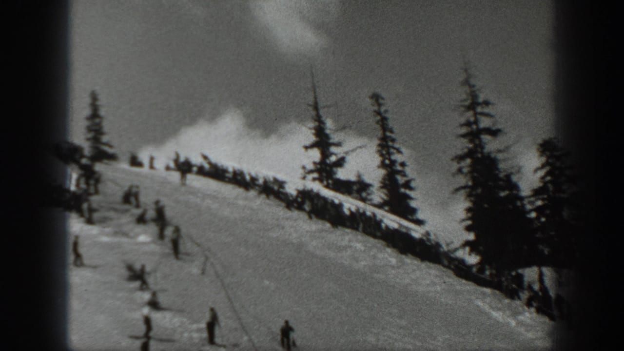 1940 Washington home-movie frame showing skiers scattered across a snowy slope below tall evergreen trees.