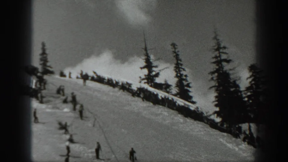 1940 Washington home-movie frame showing skiers scattered across a snowy slope below tall evergreen trees.
