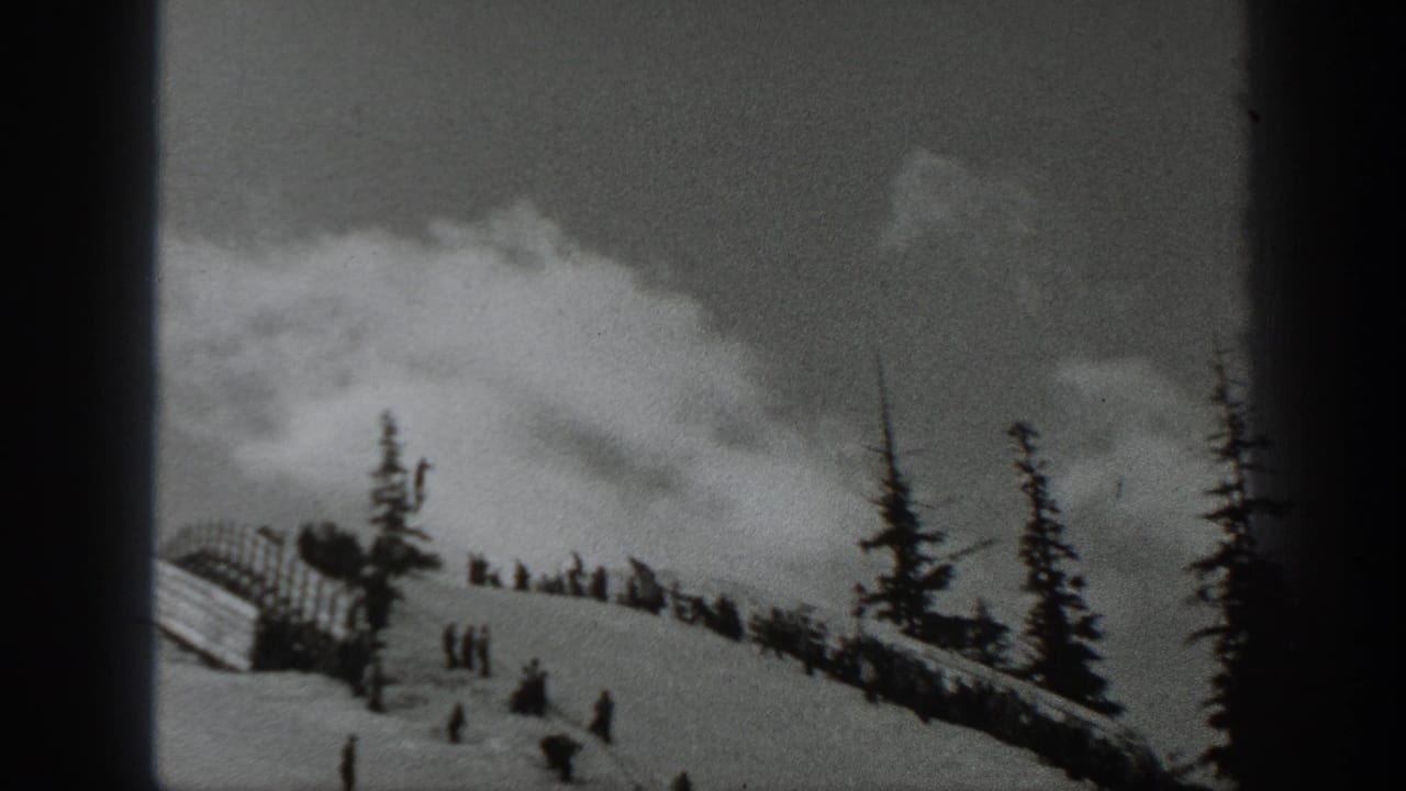 1940 Washington 8mm frame of skiers scattered across a snowy hillside with evergreen trees and a small barrier at the slope edge.