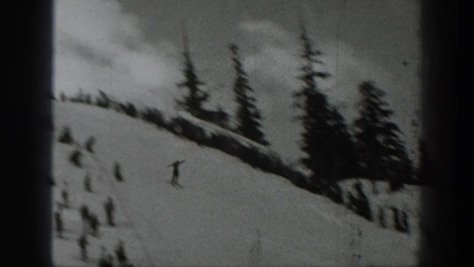 1940 Washington ski footage frame showing distant skiers on a snow-covered slope bordered by dark evergreen trees.