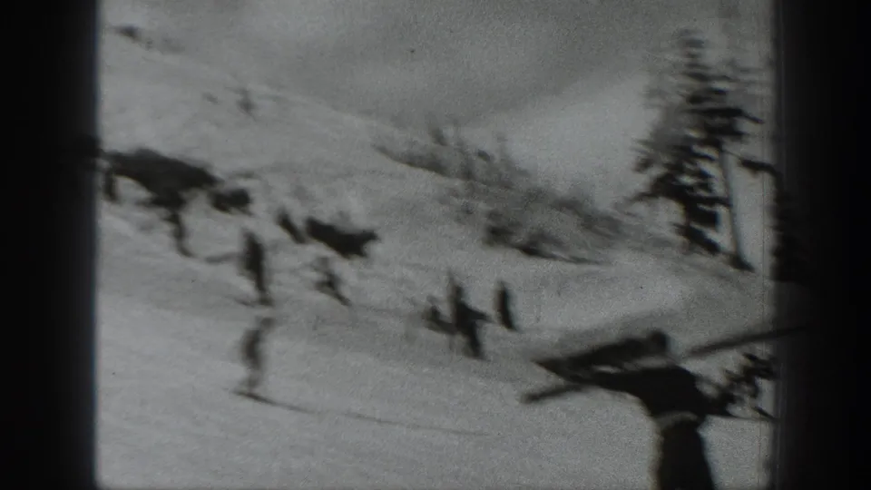 1940 Washington home-movie frame with a blurred skier in the foreground and other skiers spread across the snowy hillside.