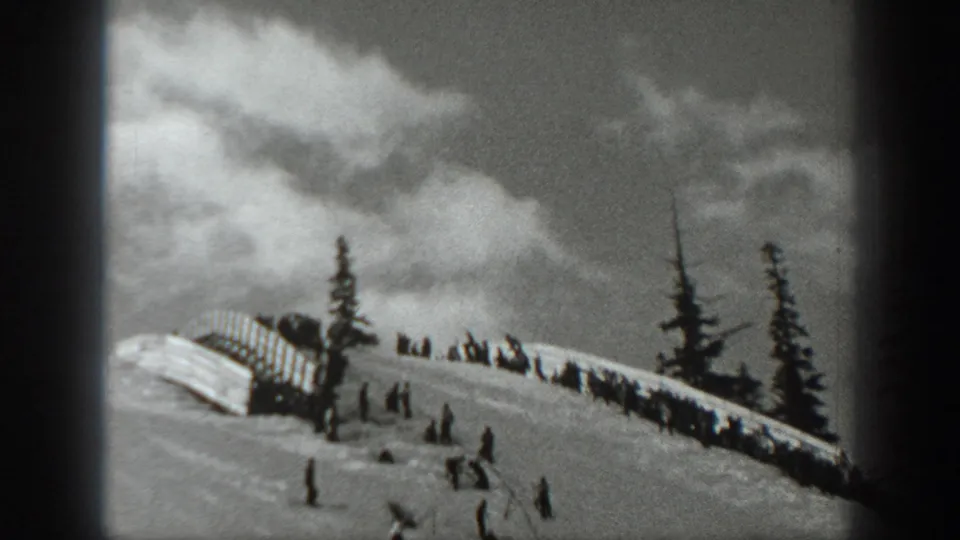 1940 Washington 8mm frame of skiers on a snowy ridge with evergreens, a small barrier, and clouded winter sky.