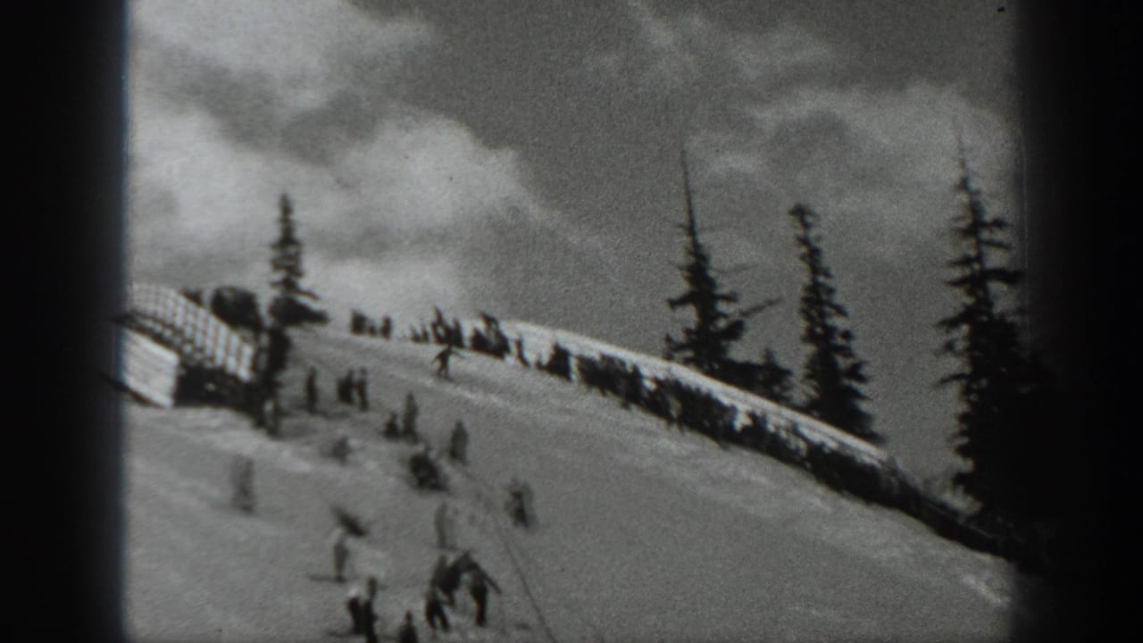 1940 Washington 8mm frame showing several distant skiers on a snowy slope beneath evergreens and a dark ridge or fence line.