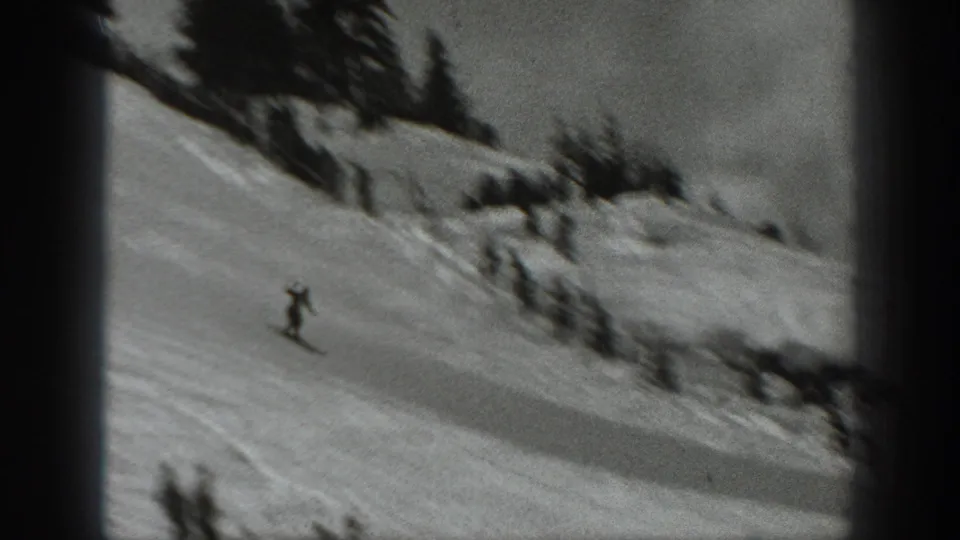 A distant skier moves downhill across a smooth snowy Washington slope, with dark trees and brush along the upper edge.