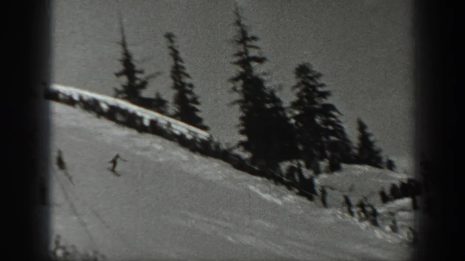 1940 Washington 8mm frame showing a distant skier on a snowy mountain slope with dark evergreens along the ridge.