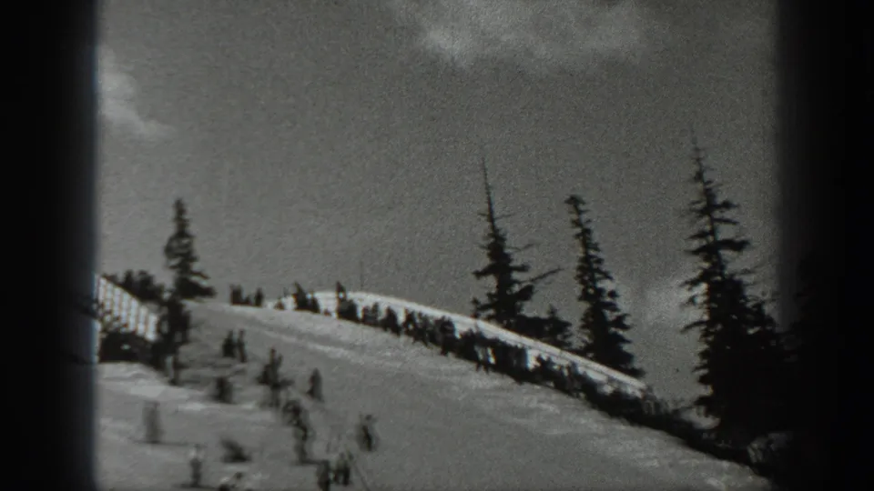 1940 Washington 8mm frame with small skiers or spectators scattered along a snowy slope below evergreen trees.