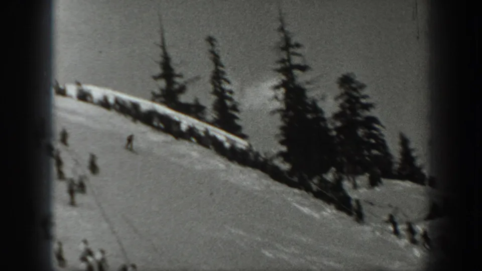 1940 Washington 8mm frame showing multiple distant skiers on a snowy run with tall evergreens in the background.