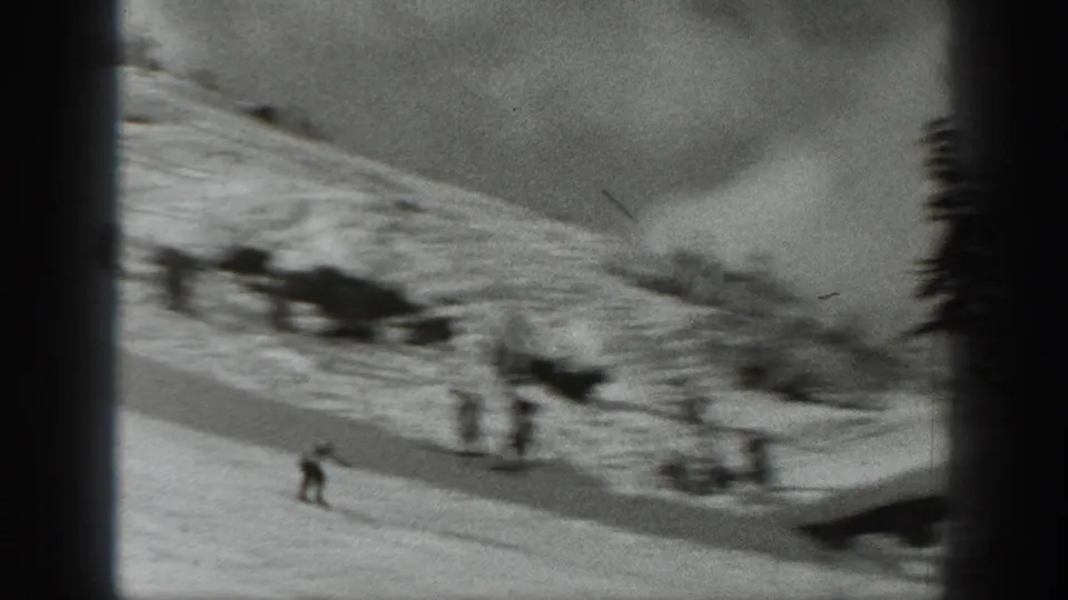 1940 Washington 8mm frame showing a wider snowy ski area with distant skiers, slope contours, and dark trees at the edge.