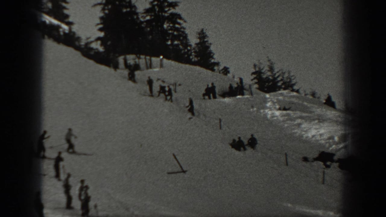 1940 Washington home-movie frame showing skiers spread across a snowy mountain slope lined with pine trees.