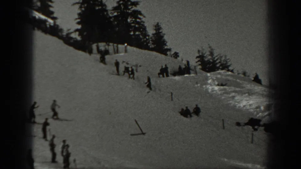 1940 Washington home-movie frame showing skiers spread across a snowy mountain slope lined with pine trees.