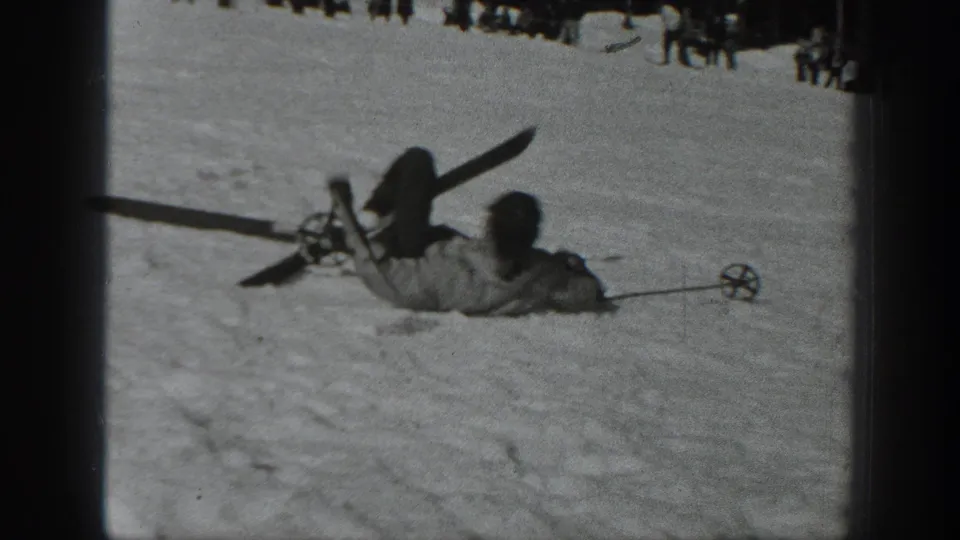 Close home-movie view of a skier who has fallen on the snowy slope, with skis and poles raised or scattered nearby.