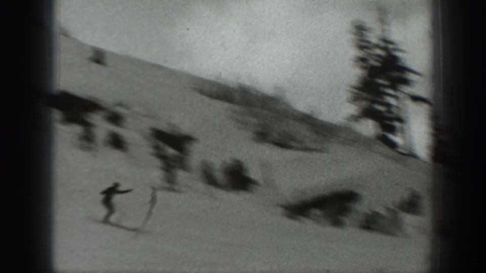 1940s Washington 8mm frame showing a skier descending a snowy slope with evergreen trees and distant skiers nearby.