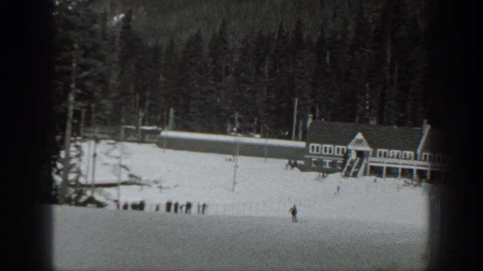 A lodge-like building beside a snowy Washington ski area, with evergreen forest and distant skiers in a 1940s 8mm frame.