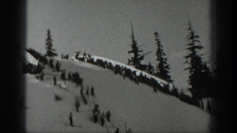 Black-and-white 8mm frame from Washington in 1940 with spectators along a snowy ridge and evergreens above the slope.