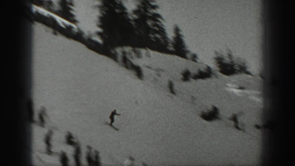 Washington 1940 frame showing a small skier moving downhill on a snowy slope with trees and spectators nearby.