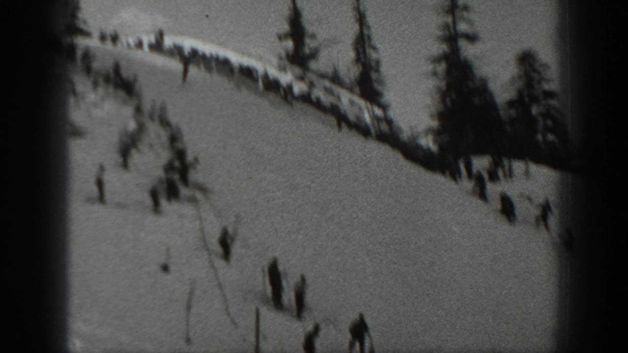 Washington 1940 home-movie frame showing a ski slope with distant skiers, spectators along a ridge, and tall evergreens.