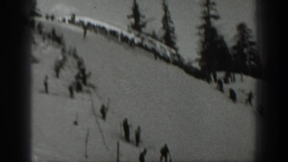 Washington 1940 home-movie frame showing a ski slope with distant skiers, spectators along a ridge, and tall evergreens.