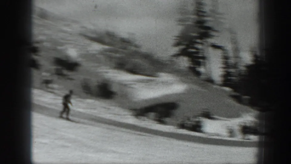 1940 Washington home-movie frame showing a skier on a snowy slope near evergreen trees and distant people.