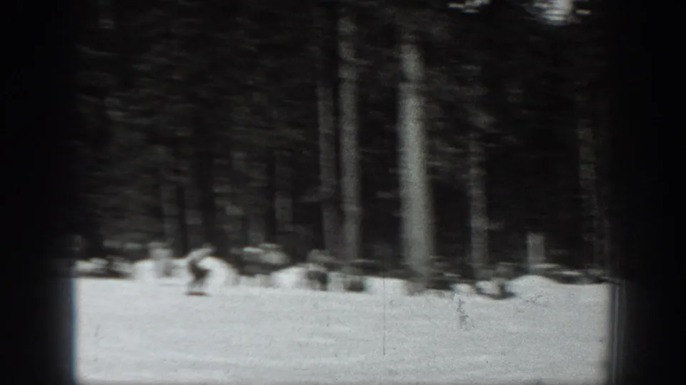 1940 Washington ski footage frame showing a skier low on the snow near a dark evergreen forest edge.