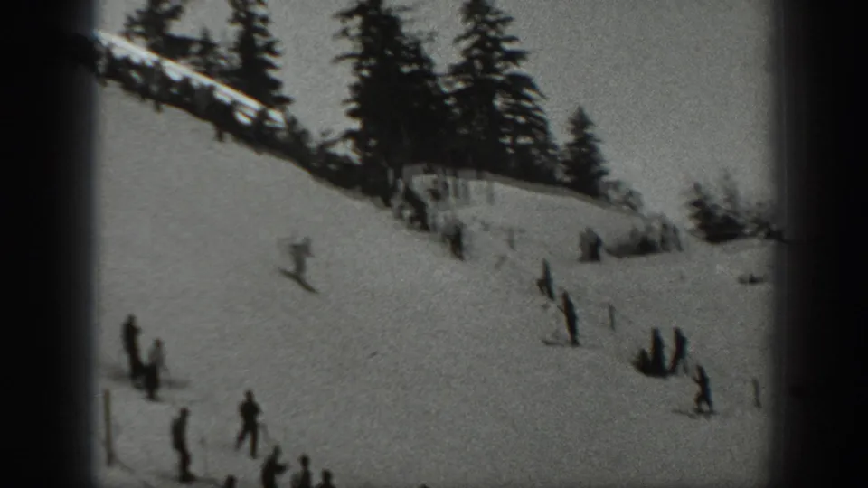 Black-and-white 1940 Washington frame with scattered skiers on an open snow slope below evergreens.