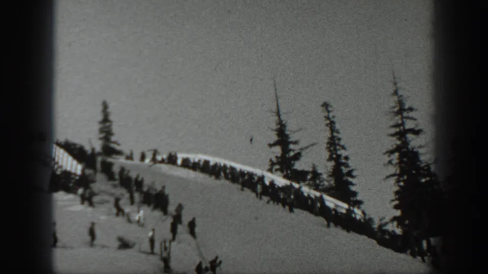1940 Washington home-movie frame showing distant skiers on a wooded snowy ridge and lower slope.