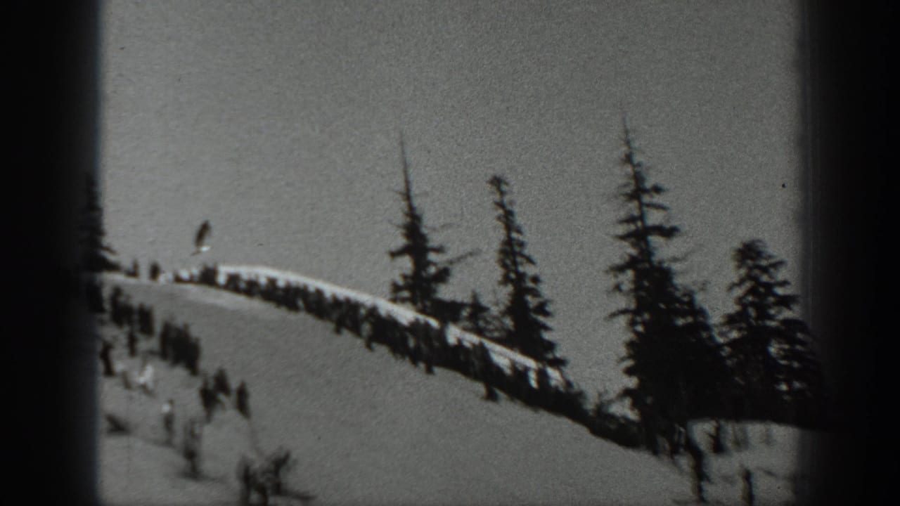 Crowd along a snowy ridge while small figures move down the mountain slope.
