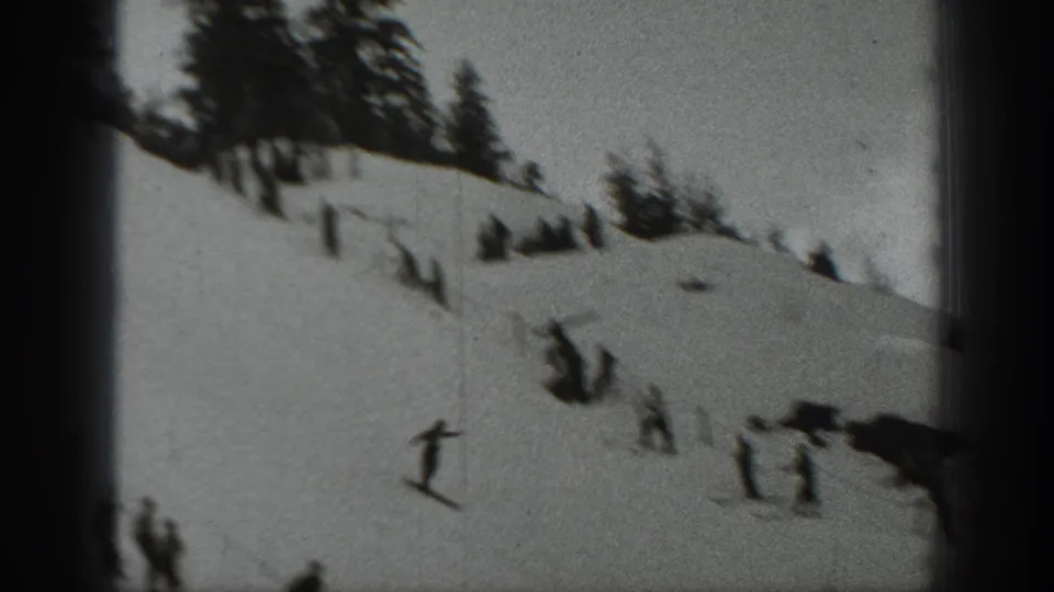 A distant skier crosses a snowy Washington slope while small spectator groups stand nearby in the 1940 home-movie frame.