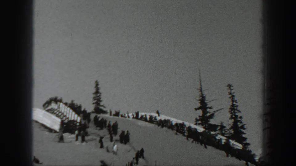 1940 Washington 8mm frame with a wooden ski-jump ramp, clustered spectators, and evergreens on a snowy hillside.