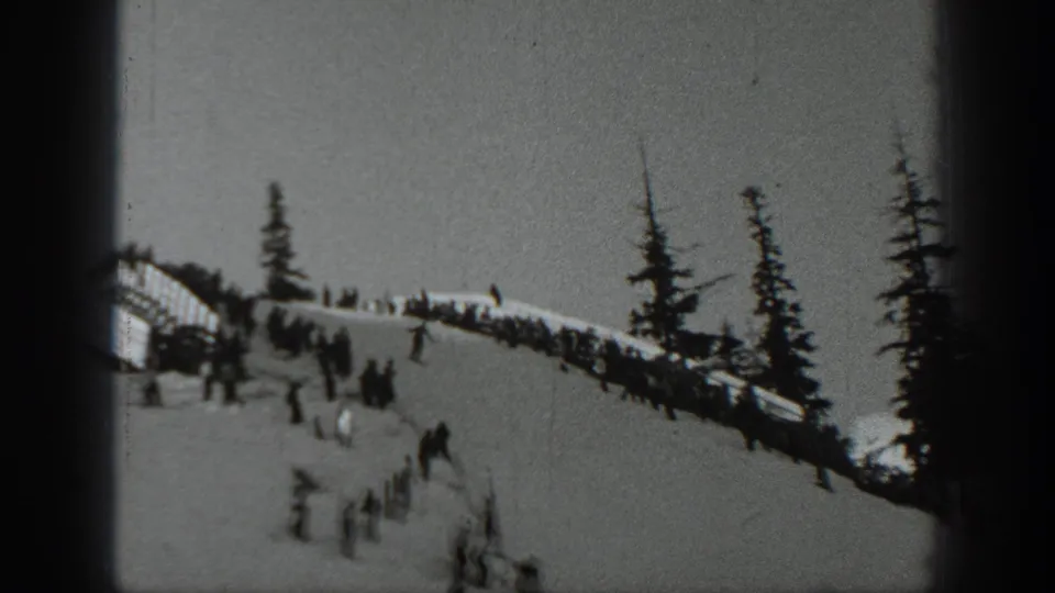 A 1940 Washington home-movie frame showing spectators and skiers gathered along a snowy ridge near dark evergreens.