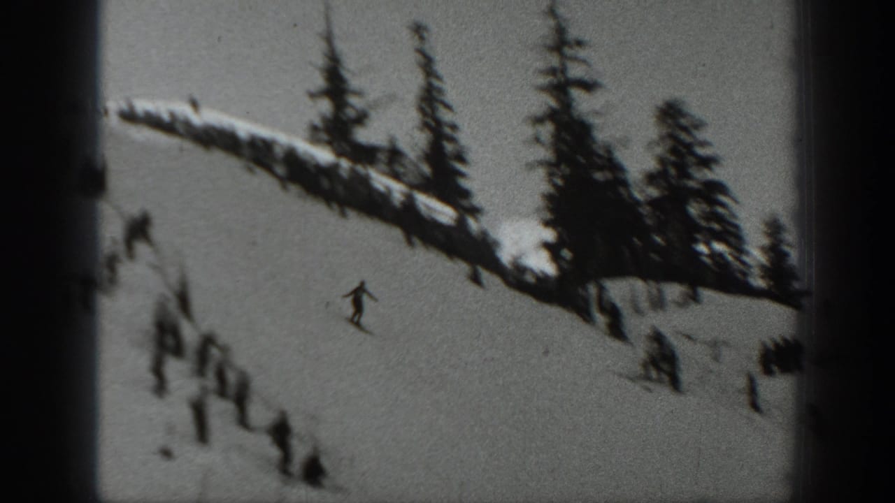 1940 Washington home-movie frame showing a snowy hillside, evergreen trees, a small skier figure, and spectators gathered along the ridge.