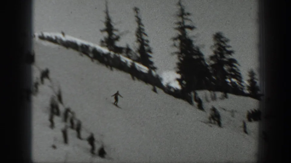 1940 Washington home-movie frame showing a snowy hillside, evergreen trees, a small skier figure, and spectators gathered along the ridge.