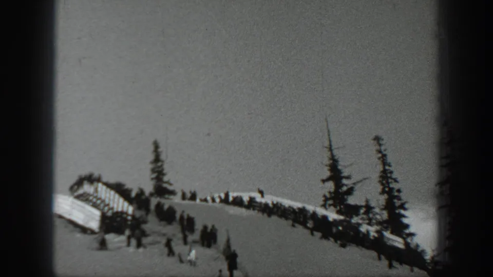 1940 Washington frame showing a ramp-like ski area, spectators along a snowy ridge, and tall evergreens on the slope.