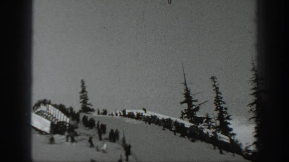 1940 Washington home-movie still with distant spectators, a ramp-like structure, and evergreen trees on a snowy winter sports slope.