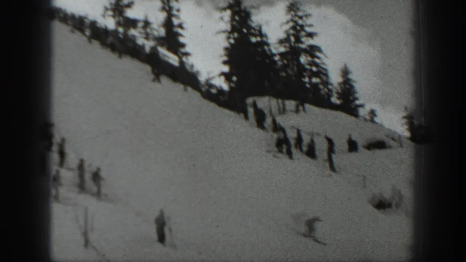 A skier crosses the lower part of a snowy Washington slope while spectators and evergreens frame the background.
