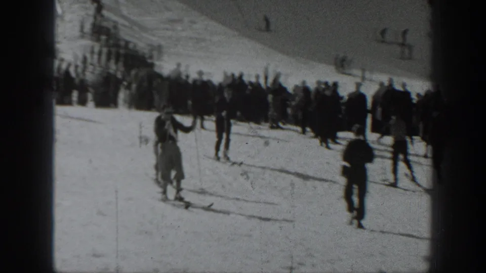 1940 Washington home-movie frame showing skiers descending a snowy slope as bundled onlookers gather near the top.