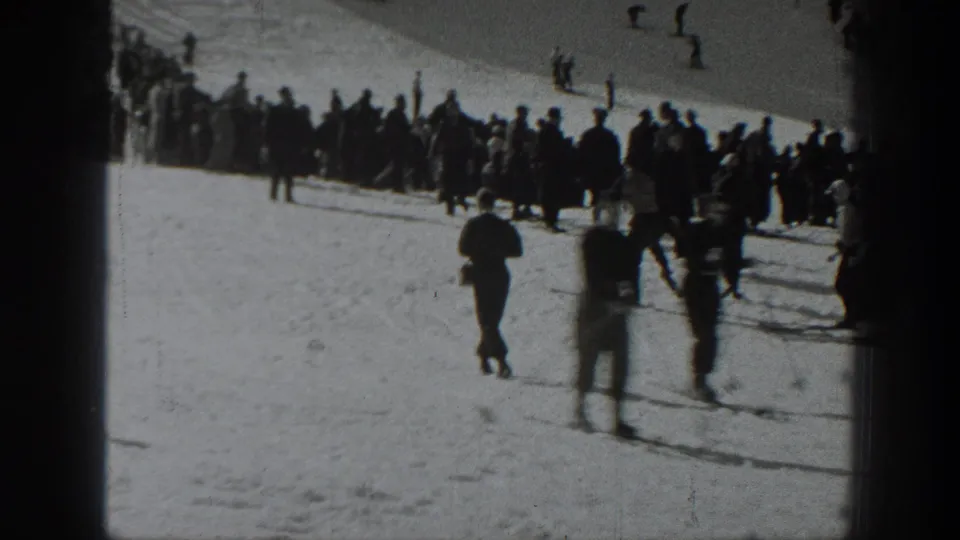 Black-and-white 8mm frame from Washington showing skiers and a bundled crowd on a sunlit snowy mountain slope.