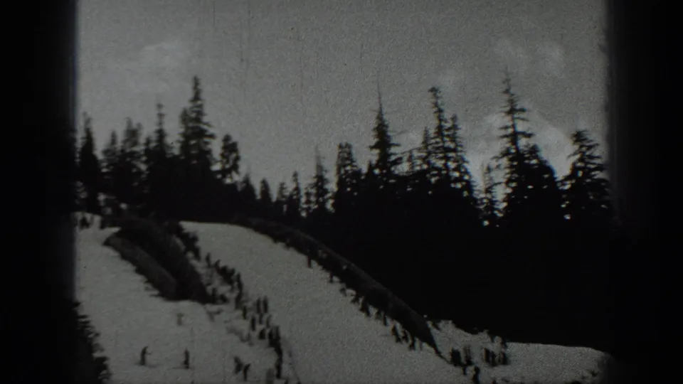 Forested Washington mountain slope with skiers appearing as small figures against snow and dark evergreens.