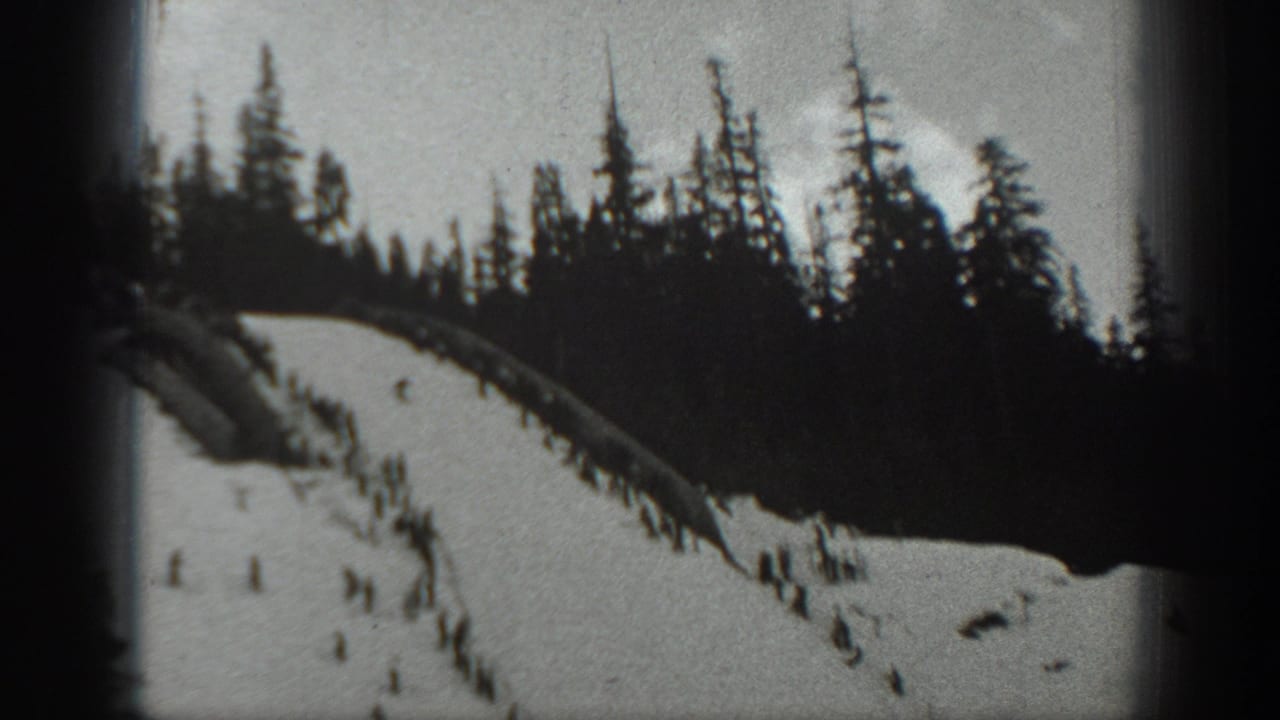 1940 Washington 8mm frame showing a steep snow-covered slope, dark pines along the ridge, and small skiers moving downhill.