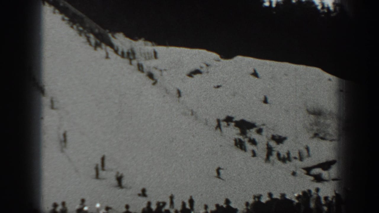 Wide snowy slope with scattered distant figures and a crowd near the bottom edge.