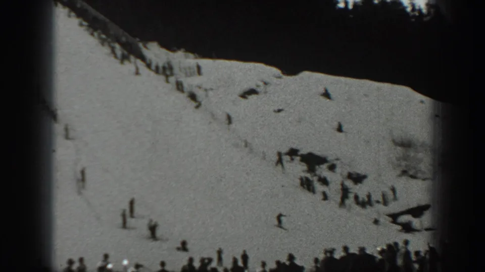 Wide 1940 Washington home-movie view of a snowy sledding hill with small figures spread across the slope and gathered below.
