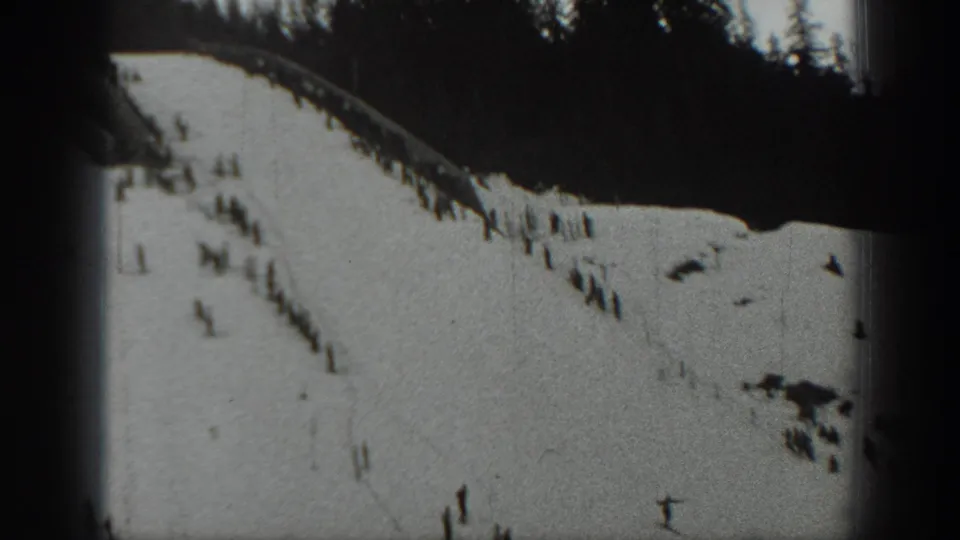 Final 1940 Washington frame of a snowy sledding slope with small silhouetted figures, evergreens, and dark patches in the snow.