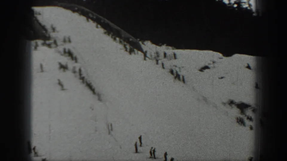 1940 Washington home-movie frame showing a snow-covered ski slope with scattered distant skiers and a dark pine treeline.
