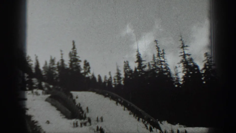 1940 Washington ski-area view with groups of distant skiers below a pine ridge on soft black-and-white 8mm footage.