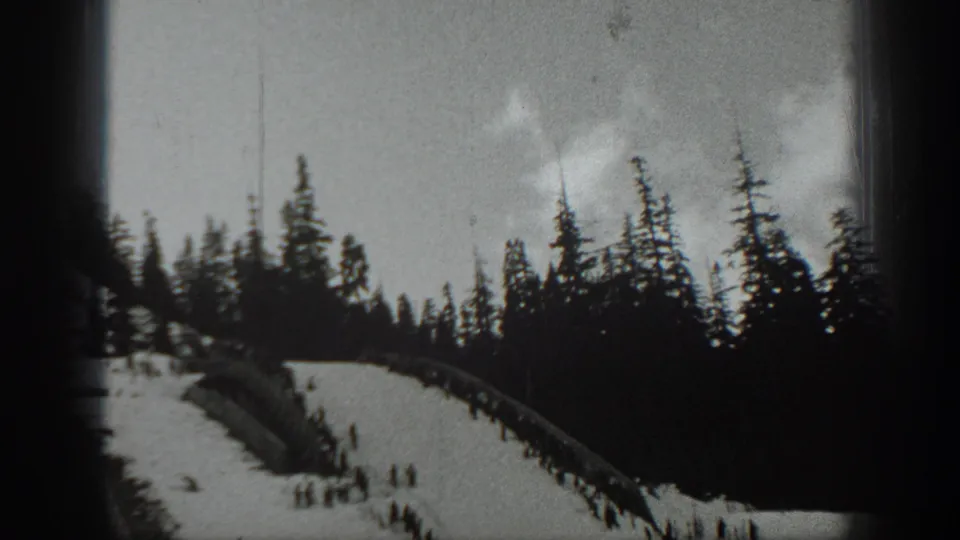 Black-and-white 8mm frame from Washington in 1940 showing a snowy ski run, dense pines, and distant people on the hill.