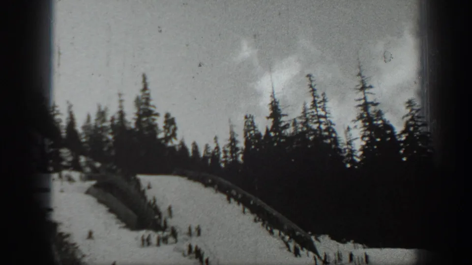 1940 Washington home-movie still of a tree-bordered ski slope with distant skiers gathered near the bottom of the frame.