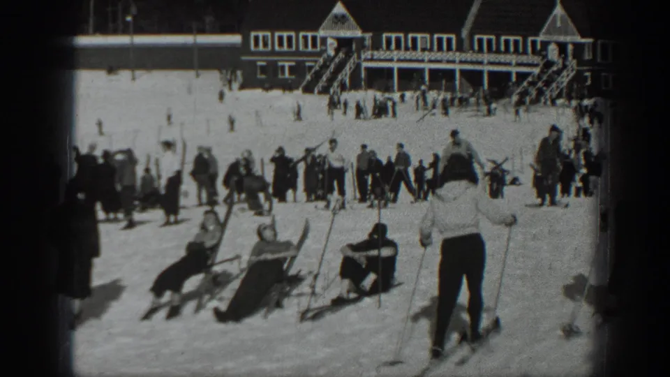 1940 Washington home-movie frame showing skiers and onlookers gathered on snow near a large resort lodge.