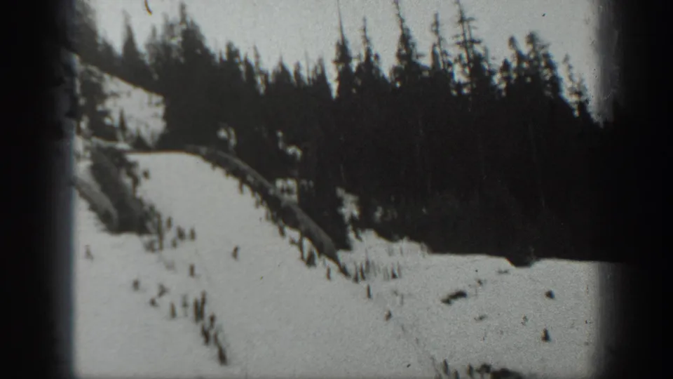 1940 Washington ski-resort frame showing a broad snowy slope, tree line, and distant skiers.