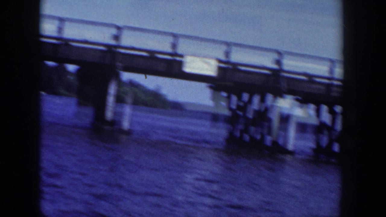1953 Wisconsin home-movie frame showing a metal bridge crossing water, seen from below with shoreline in the distance.
